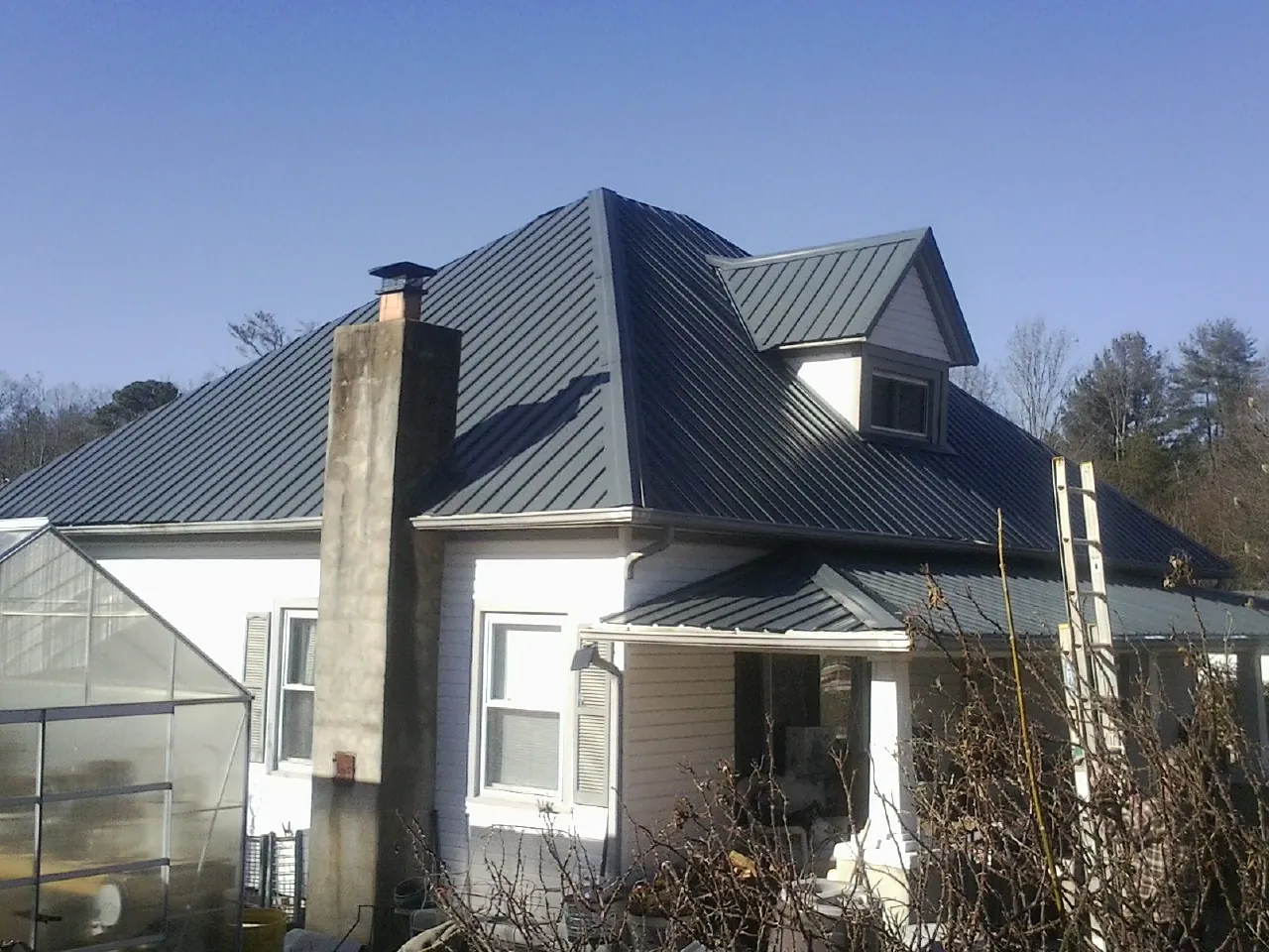 Dark blue standing seam metal roof on a white farmhouse with dormer — Slate & Tile Roof Repair by Roofing Brothers in Blairsburg