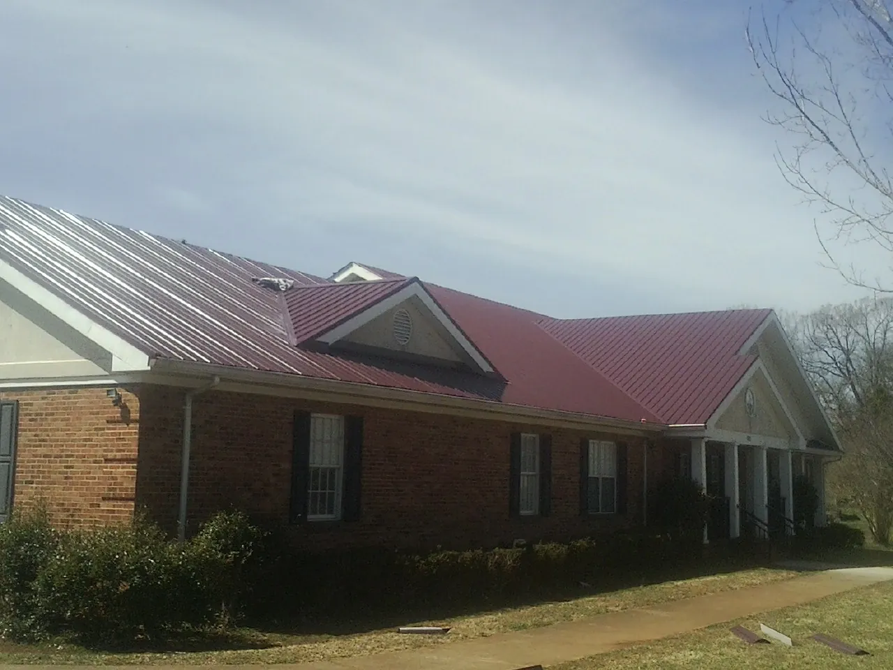 Red metal roof with gabled entries on a long brick building, from a Hail Damage Roof Repair job in Blairsburg