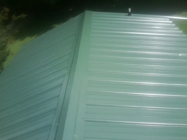 New green metal panels meeting at the ridge of a roof — Flat Roof Repair work by our crew in Blairsburg