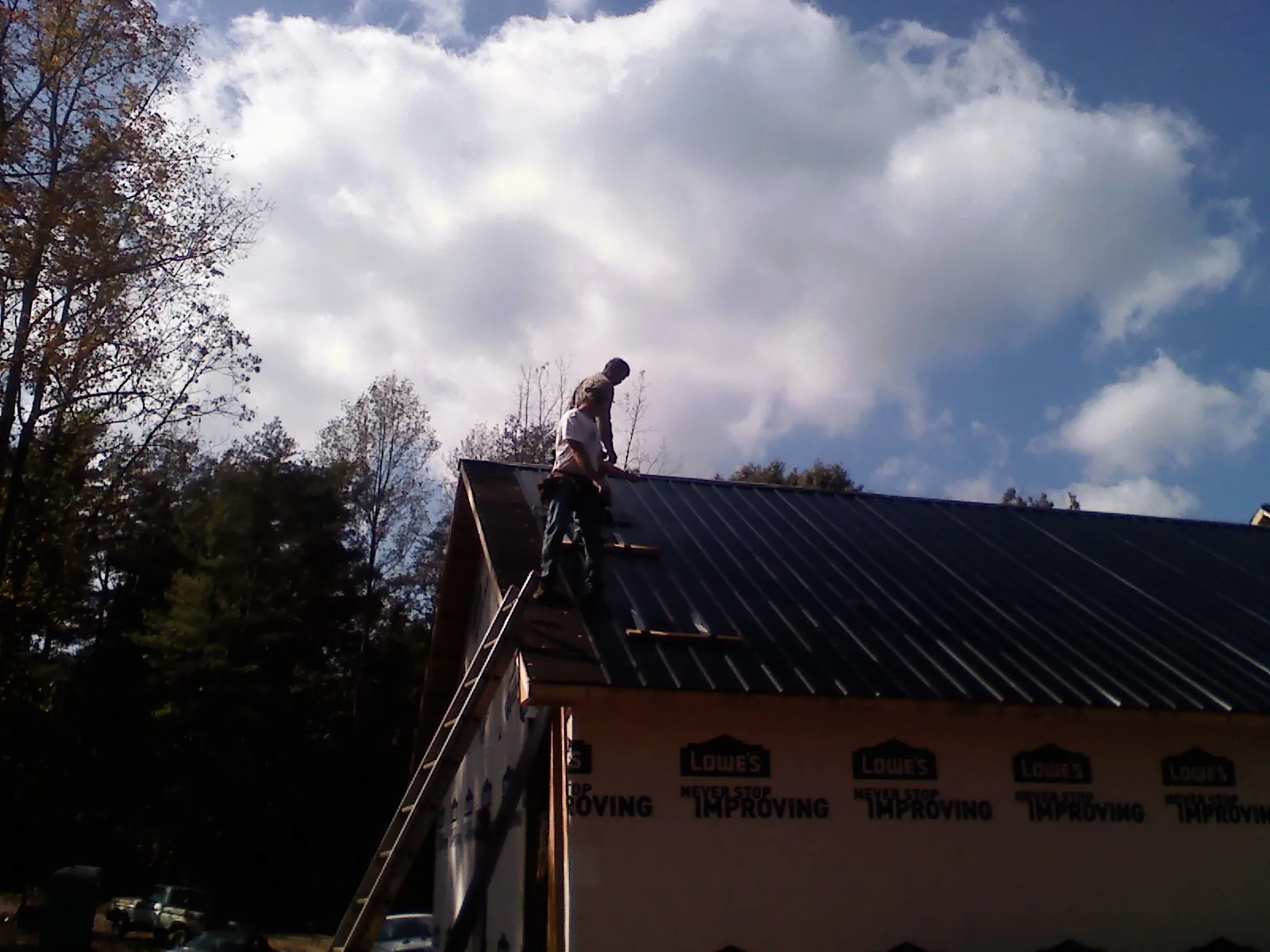 Roofer fastening dark metal panels high against a cloudy sky, from a Roof Inspection job in Blairsburg
