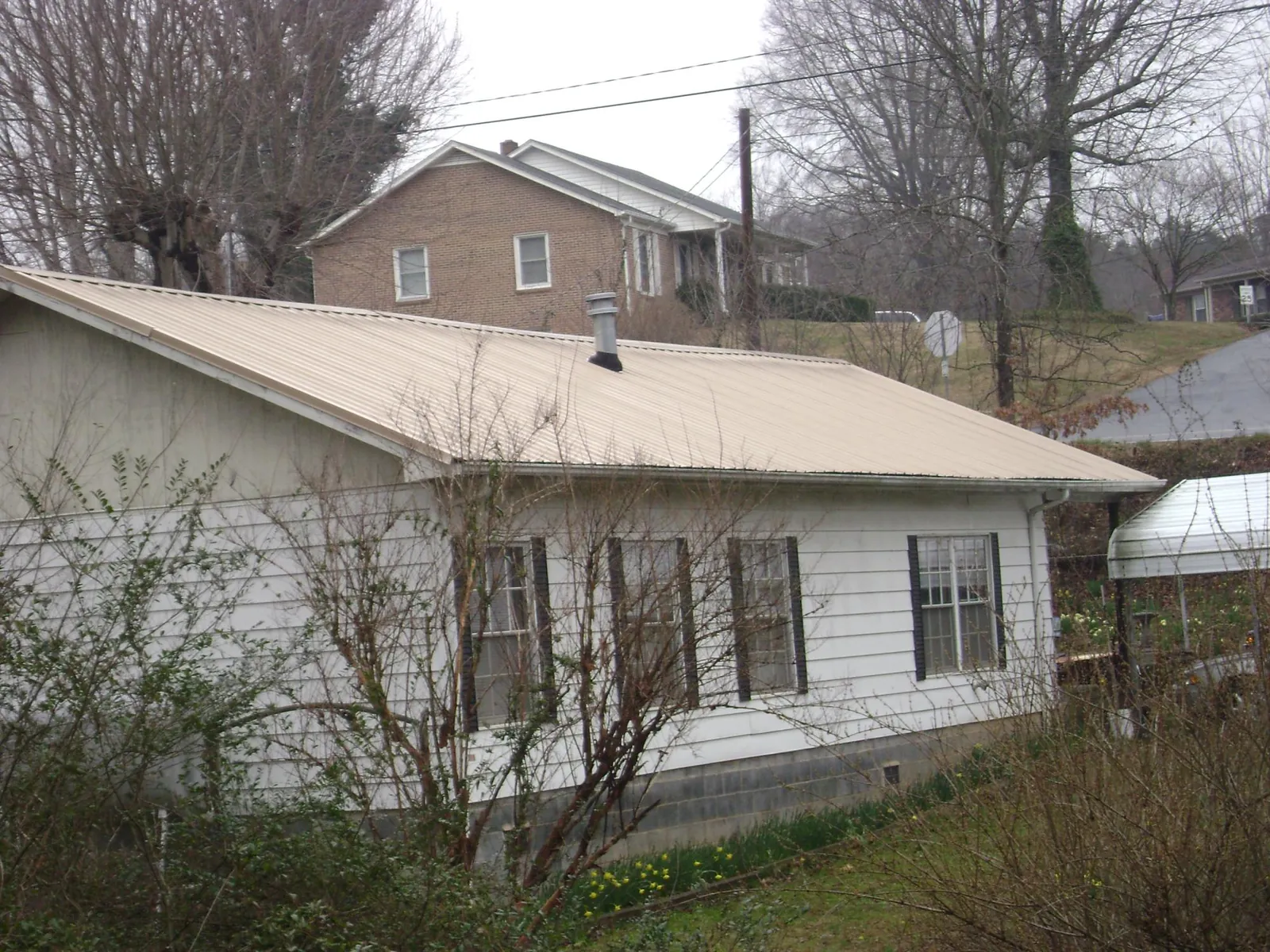 Tan metal roof on a white sided house set into a hillside — Commercial Roofing by Roofing Brothers in Blairsburg